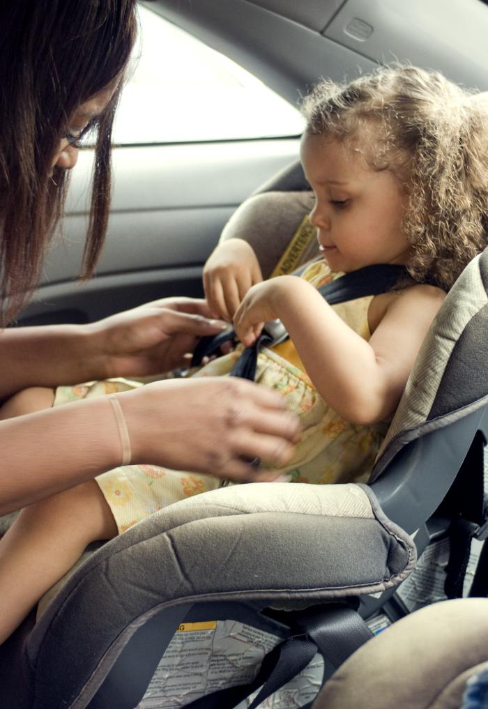 A woman buckles a young girl into her car seat.